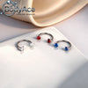 A pair of titanium steel nose rings featuring red and blue cubic zirconia crystals displayed on a white surface.