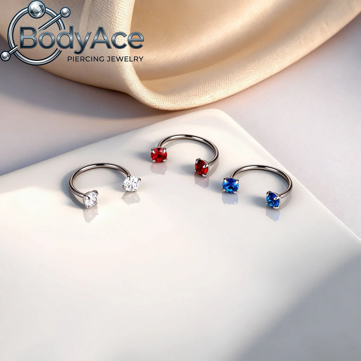 A pair of titanium steel nose rings featuring red and blue cubic zirconia crystals displayed on a white surface.