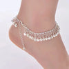 A delicate silver bell foot chain anklet worn around a slender ankle.