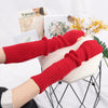 A close-up of a red knitted fingerless glove worn on a hand, displayed next to some floral elements.