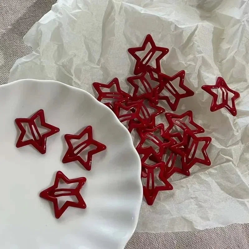 A collection of red star snap clips for hair and barrettes displayed on a white plate against crumpled paper.