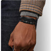 Nahaufnahme eines Mannes Handgelenks mit einem schwarzen geflochtenen Lederarmband, sichtbar gegen ein dunkles Hemd und einen