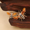 Broche ton or avec des motifs de abeille et d'insectes baroques sur une surface en bois sombre.