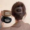 A hand is holding a matte brown oval hair claw clip and a matte black oval hair claw clip against a person's dark hair.