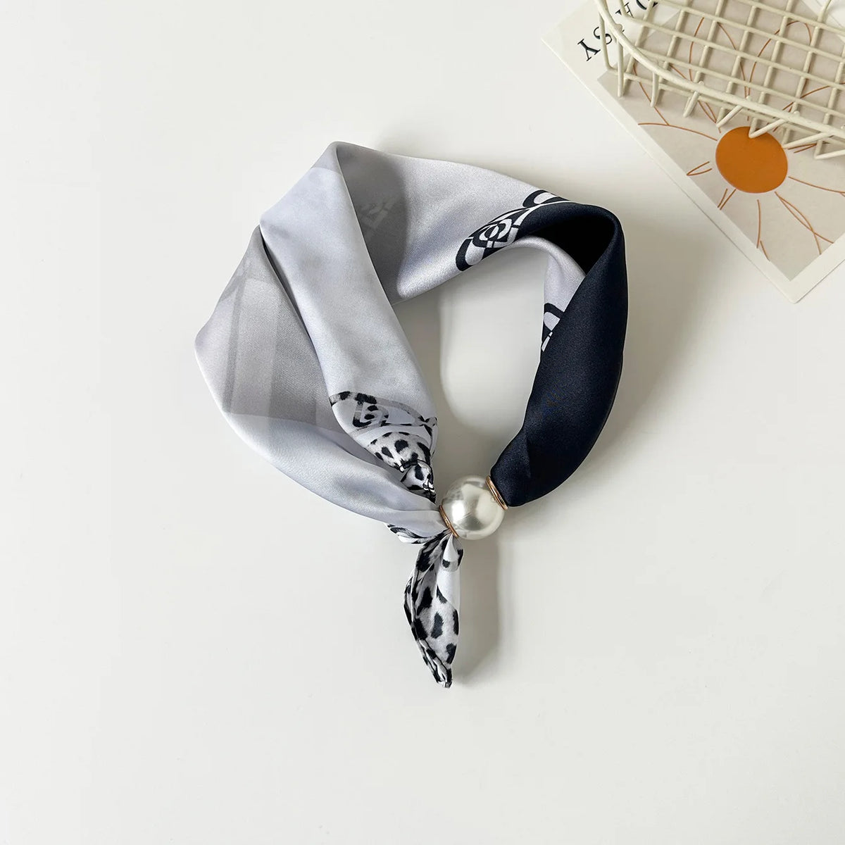 A silk scarf featuring a gray and black leopard print tied with a pearl knot.