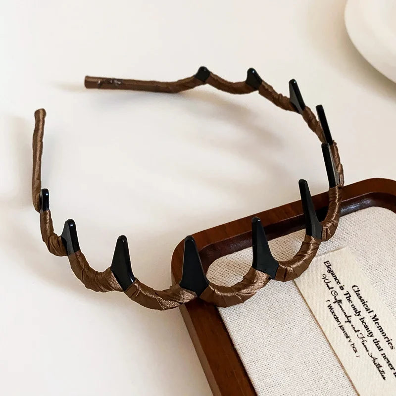 A brown resin wave toothed headband for women displayed on a wooden tray.
