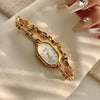 A gold-toned quartz fashion wristwatch is displayed on a light fabric next to manicured fingers.