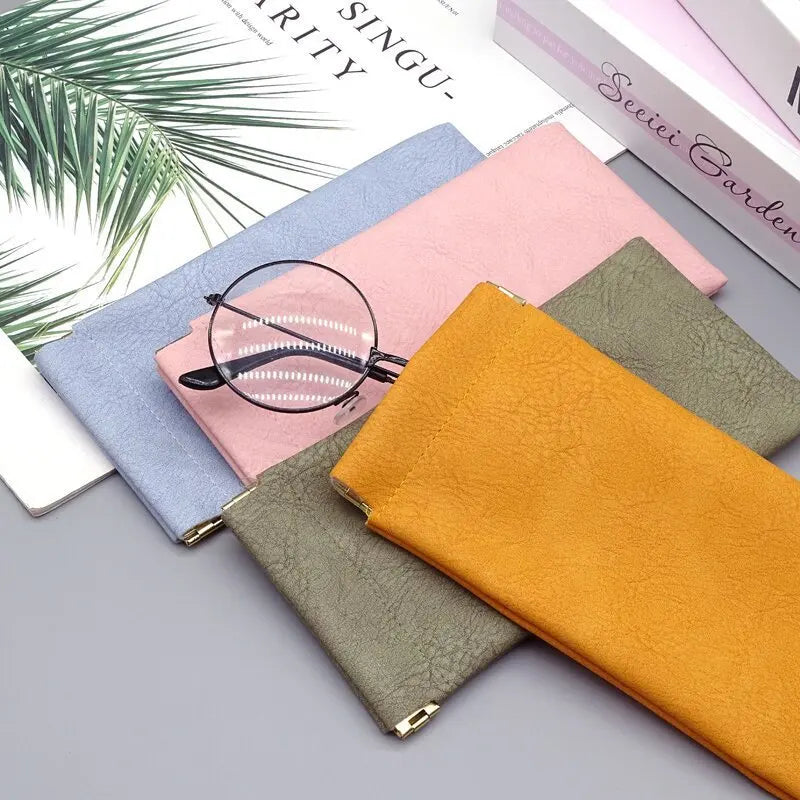 A collection of pink, blue, and olive green PU leather eyewear storage bags with a pair of eyeglasses resting on top.
