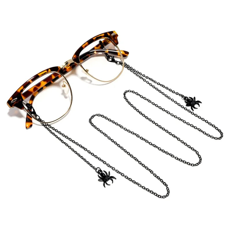A pair of tortoiseshell sunglasses with a chain necklace featuring small black spider charms.