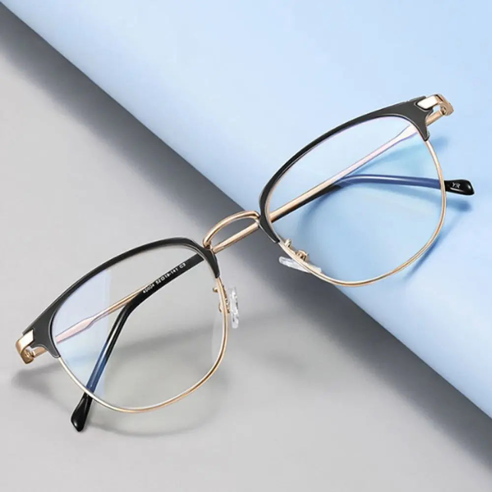 A pair of gold-toned metal eyeglasses with thin frames and clear lenses resting on a light blue surface.