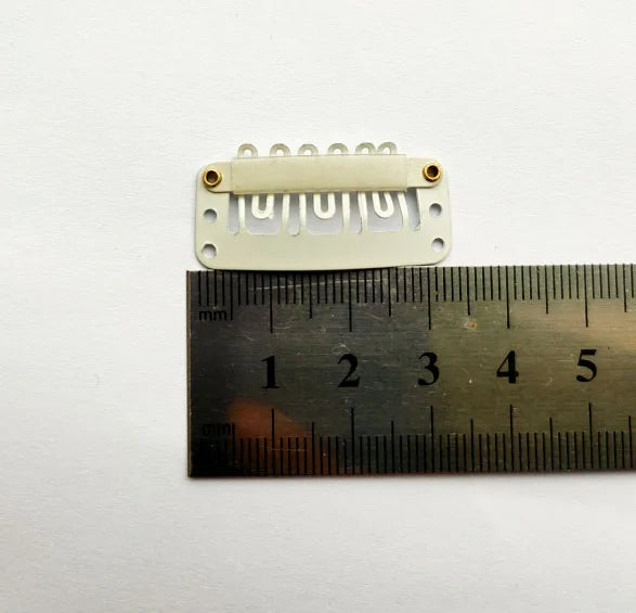 Une pince d'extension de cheveux blanche de précision avec de petites dents est montrée à côté d'une règle.