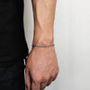 A close-up of a stainless steel twisted chain bracelet worn on a wrist against a dark shirt.