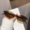 A pair of brown retro oval frame sunglasses resting on a white surface, held by a hand wearing a white fluffy sleeve.