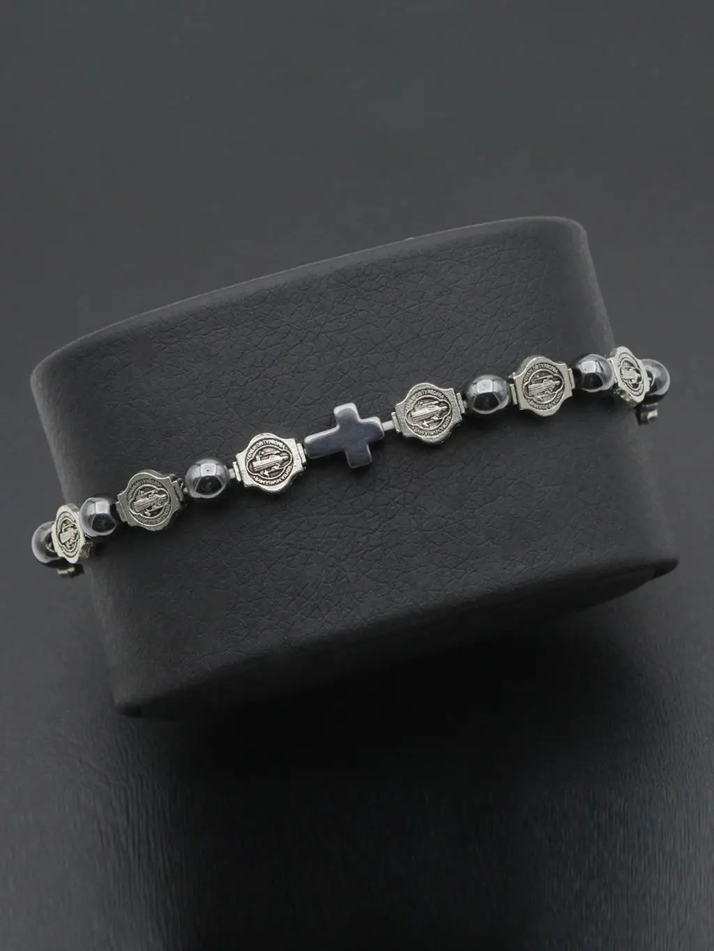 Rosario de plata con pequeños dijes decorativos y una cruz sobre una superficie oscura.