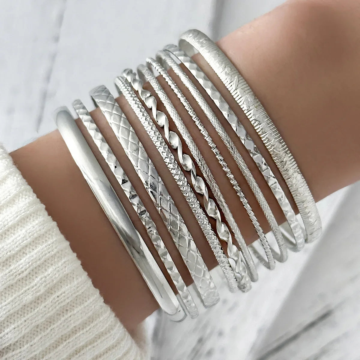 A stack of silver twisted bangle bracelets worn on a wrist.