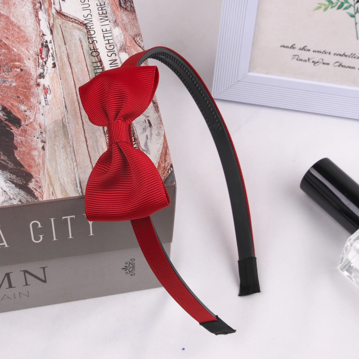 A red grosgrain ribbon hair bow is displayed next to a box and a framed card.