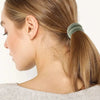 A woman is shown with her hair pulled back in a ponytail using a green elastic hair band.