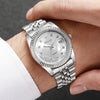 A silver wristwatch with a crystal face and metal band is worn on a person's wrist.