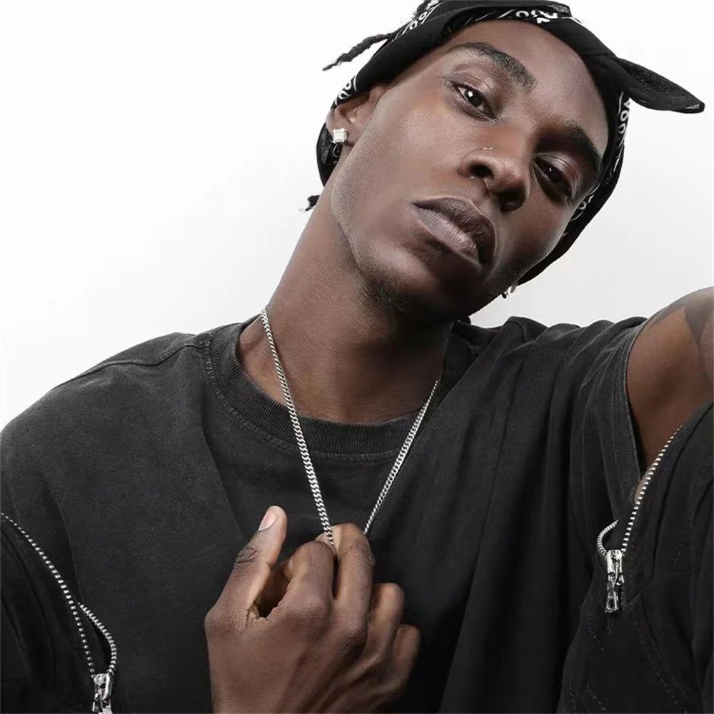 A close-up photo of a man wearing a silver stainless steel Cuban chain necklace and a black t-shirt.