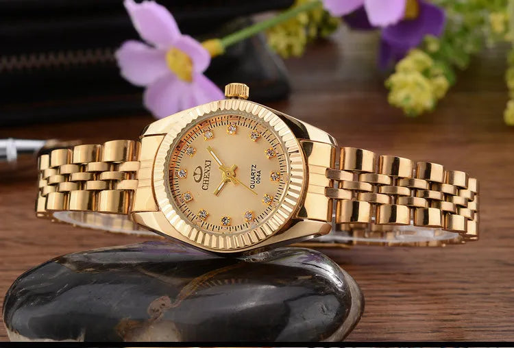 A luxury golden quartz wristwatch with a gold-toned band rests on a dark stone surface.