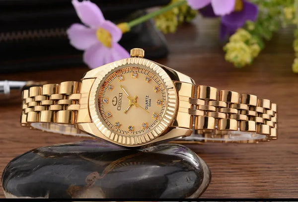 A luxury golden quartz wristwatch with a gold-toned band rests on a dark stone surface.