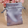 A lavender satin drawstring pouch tied with a matching ribbon, resting on a beige fabric next to pink flowers.
