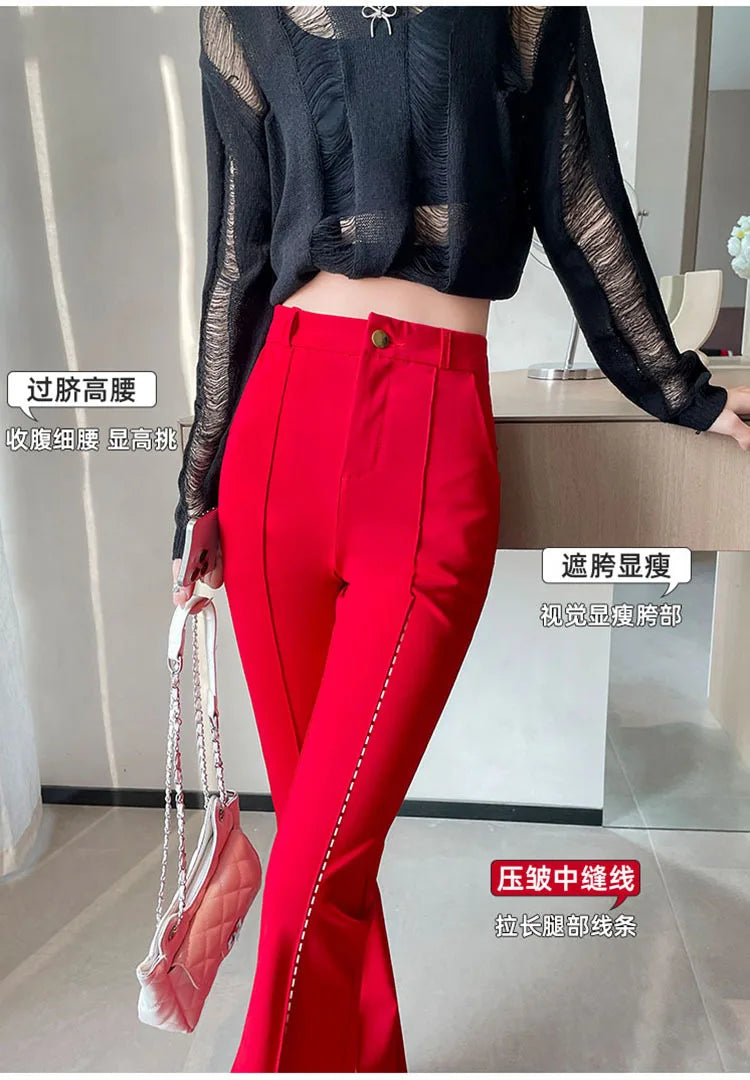 A woman models bright red high-waist flare skinny pants with sheer black long-sleeved top and a handbag.