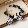 A black and white patterned fabric headband tied in a bow, displayed on a light wooden surface.