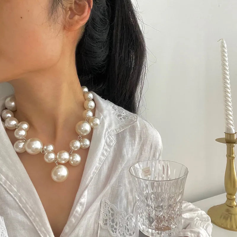 A close-up of a woman wearing an elegant simulated pearl choker necklace with a white blouse.