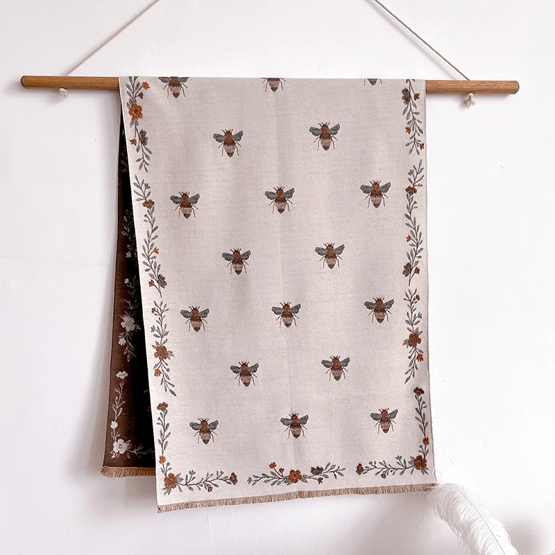 A beige pashmina shawl featuring a floral print of small bees and dried foliage.
