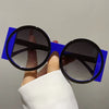 A hand holds a pair of round double color fashion sunglasses with blue frames and black lenses.