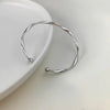 Silver twisted wave cuff bracelet displayed on a white ceramic dish.
