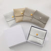 A set of elegant PU leather jewelry pouches in beige and gray colors with gold snap buttons displayed next to a white box.