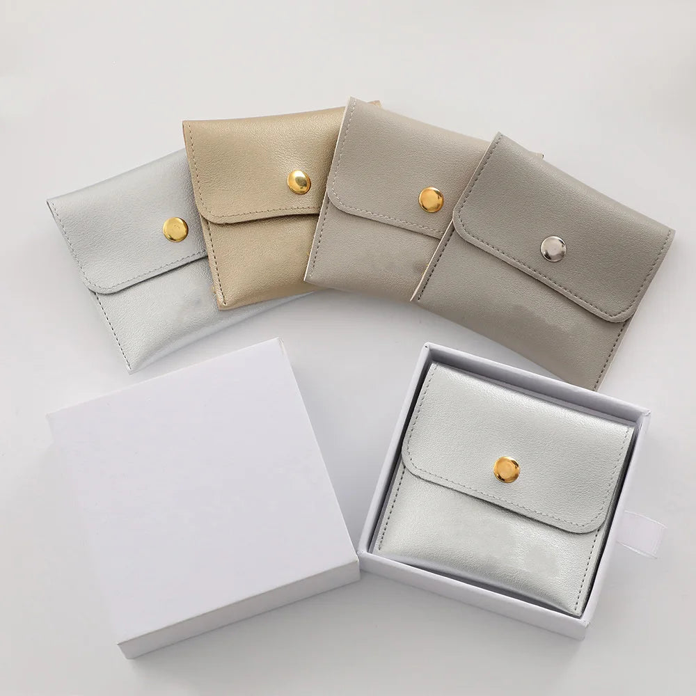 A set of elegant PU leather jewelry pouches in beige and gray colors with gold snap buttons displayed next to a white box.