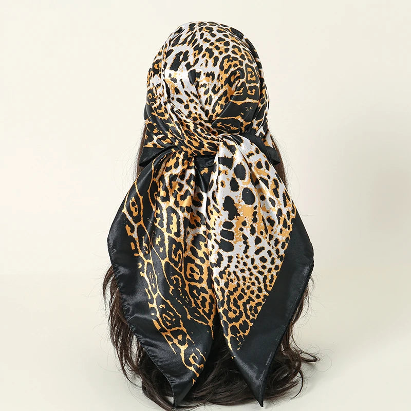 A black and gold leopard print satin silk scarf tied around a woman's dark hair.