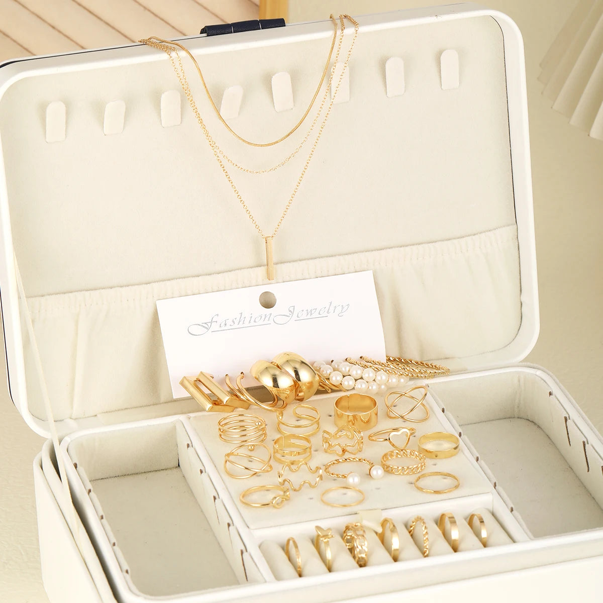 Une boîte à bijoux ouverte présentant un ensemble de bijoux géométriques en or, avec colliers et bagues.