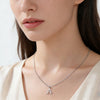A silver initial letter necklace worn by a woman's neck and chest.