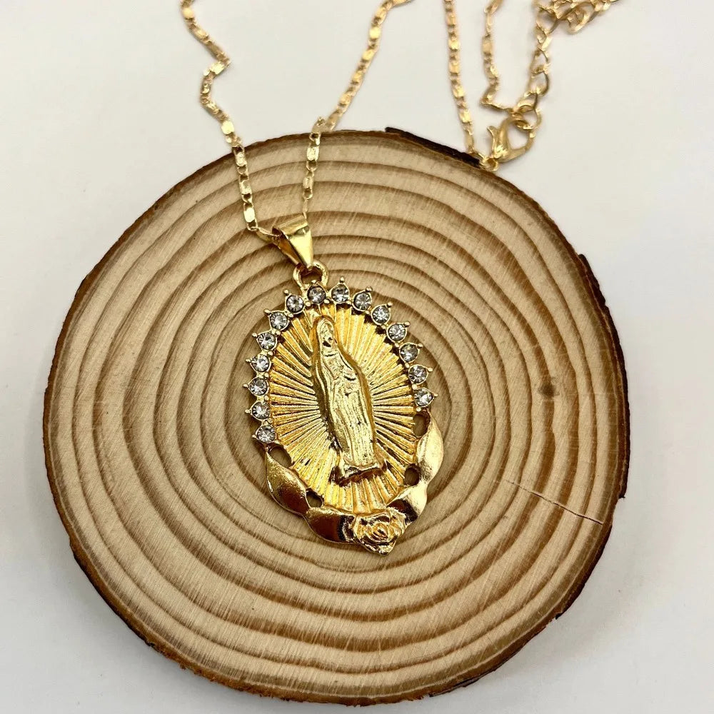 A dainty golden Christian necklace featuring a figure set in a sunburst design, displayed on a wooden slice.