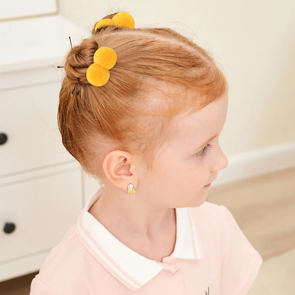 A toddler with reddish hair is wearing yellow plush elastic hair bands on top of her head.