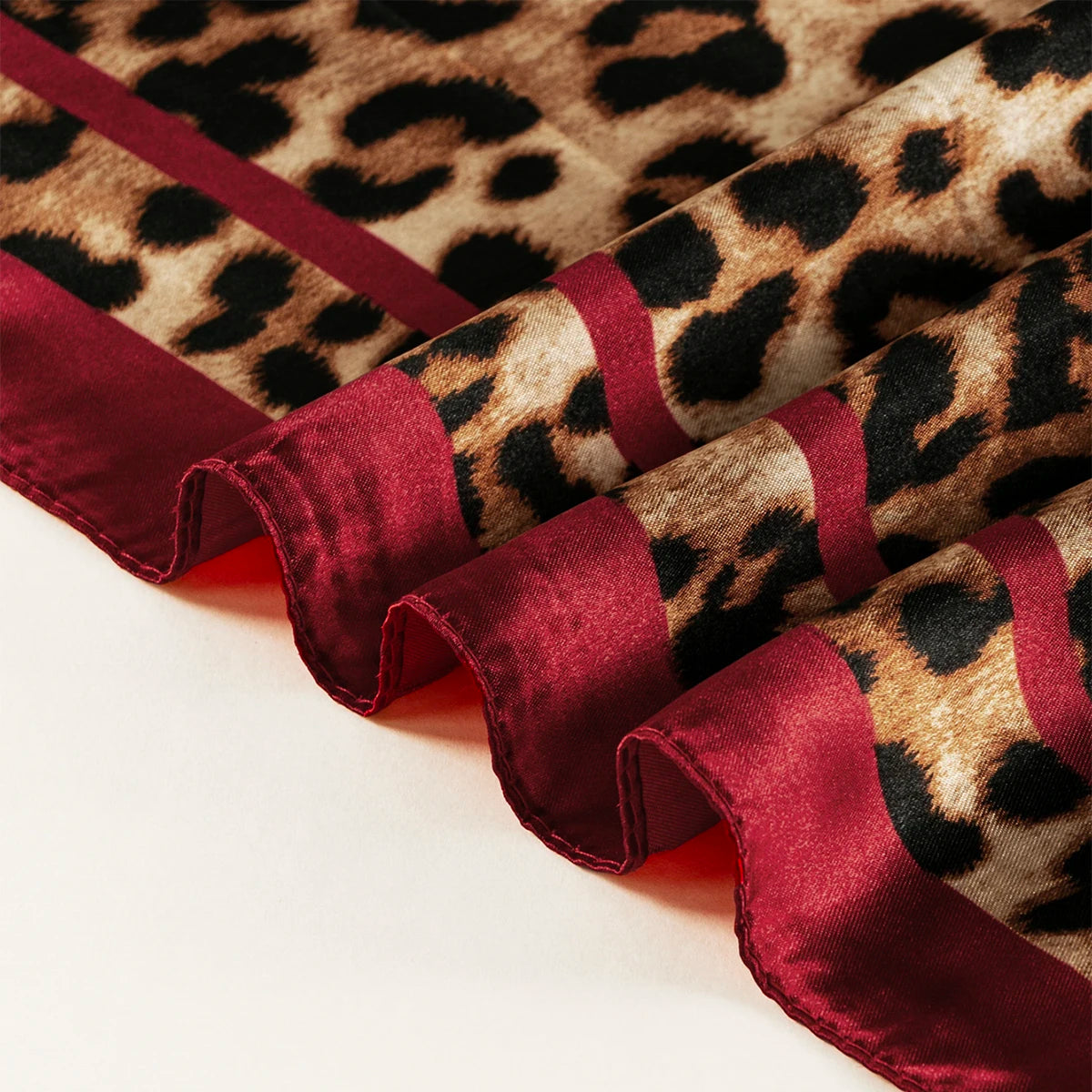 A close-up of a deep burgundy satin scarf featuring a leopard print pattern.