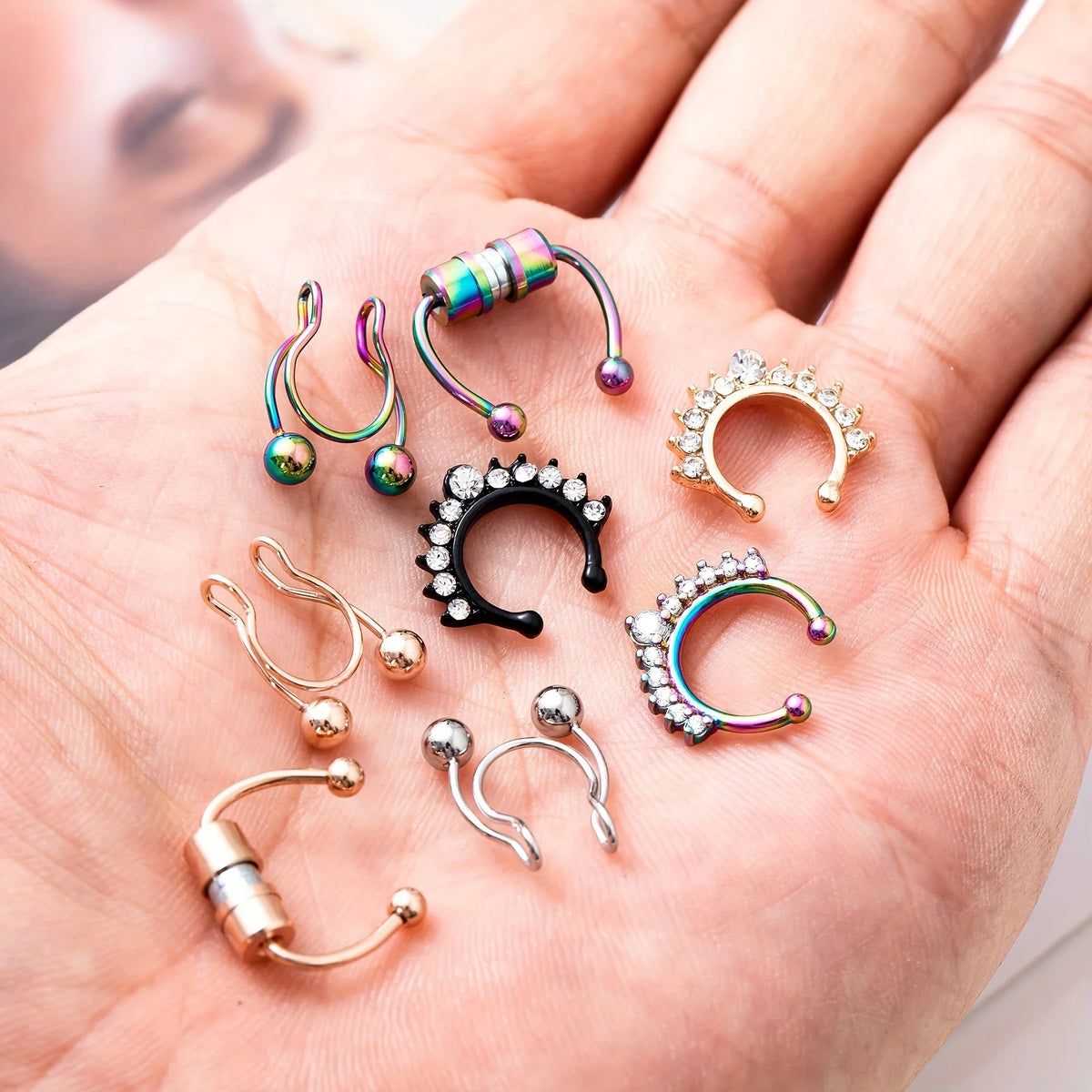 A hand holds a collection of magnetic stainless steel septum rings in various finishes and styles.