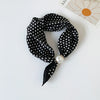Black silk scarf with white polka dots tied in a bow and secured with a pearl bead.
