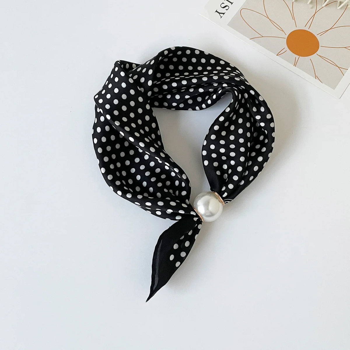 Black silk scarf with white polka dots tied in a bow and secured with a pearl bead.