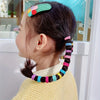 A young girl shows off her dark hair styled with colorful nylon elastic hair cords and a floral headband.