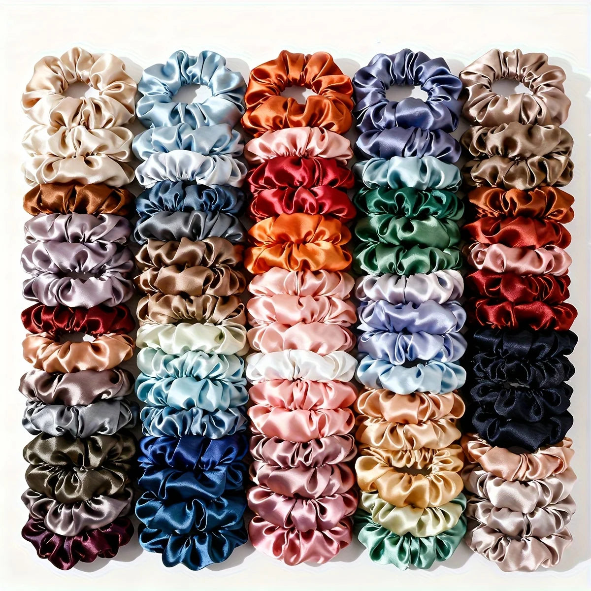 A set of five satin hair scrunchies in various shades of pink, purple, green, and brown.