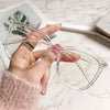 A hand holds a pair of clear, large square anti-blue light spectacles on a marble surface.