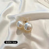 A pair of gold-toned simulated pearl hair claws displayed on a white satin fabric.