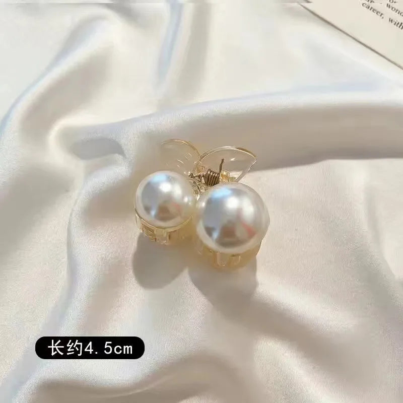 A pair of gold-toned simulated pearl hair claws displayed on a white satin fabric.