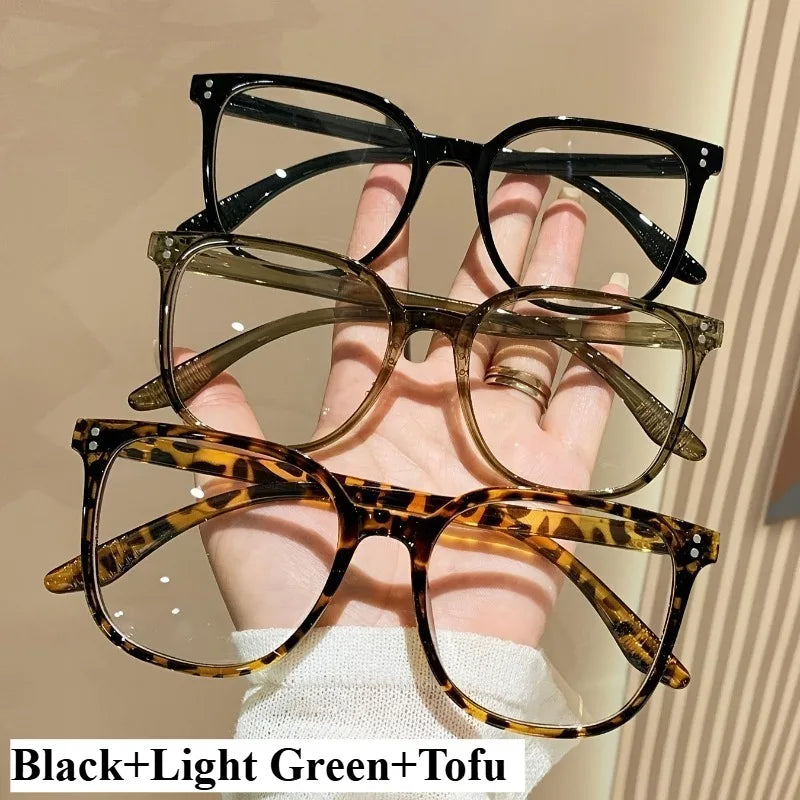 A set of black, light green, and tofu-colored classic square anti-blue light eyeglasses being held by a hand.