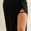 A close-up of a woman wearing a black dress, showcasing boho crystal leg thigh body chain jewelry on her skin.
